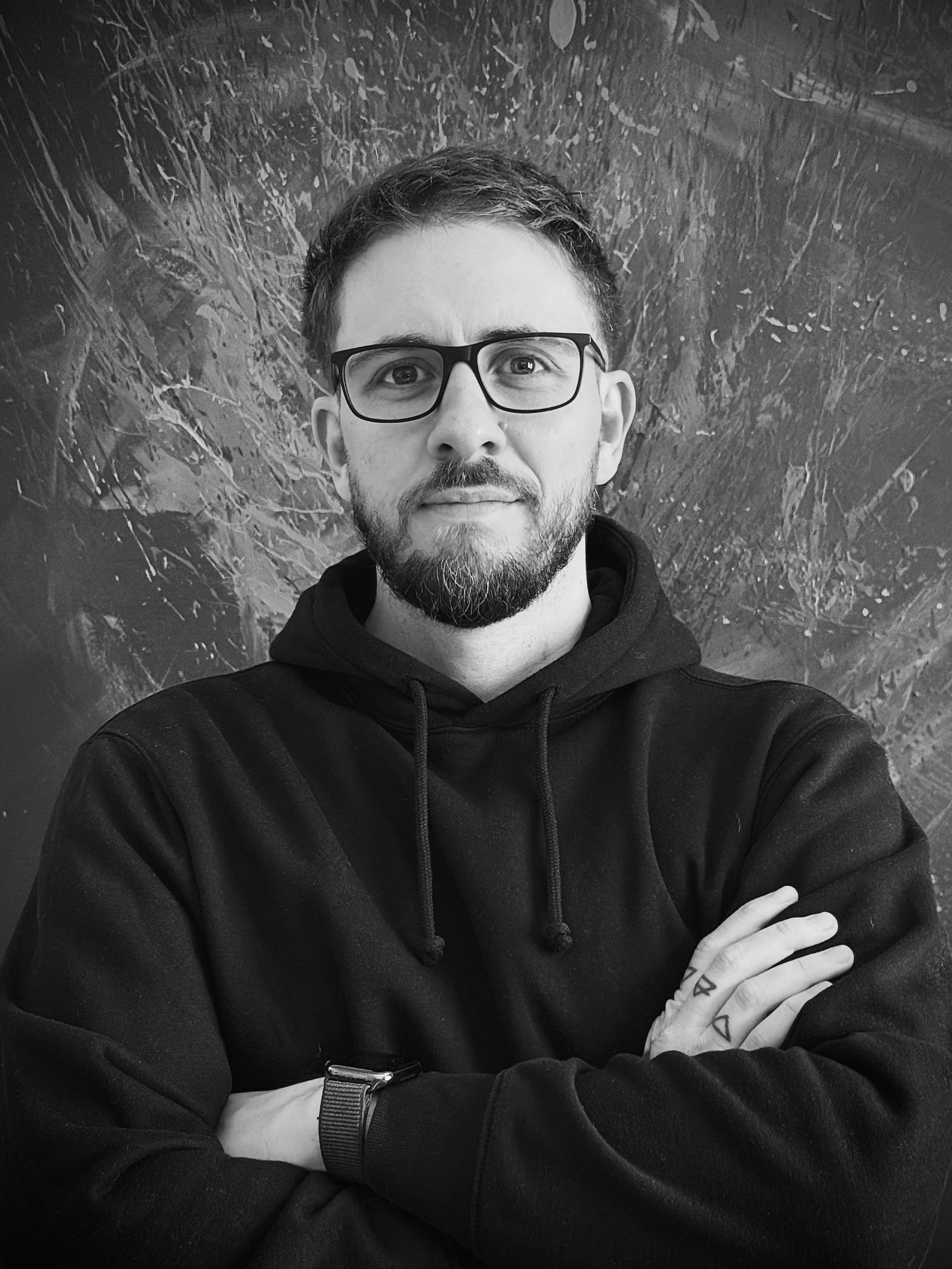 Gregor Schmidinger mit verschränkten Armen vor einem Bild mit Farbspritzern, schwarzweiß