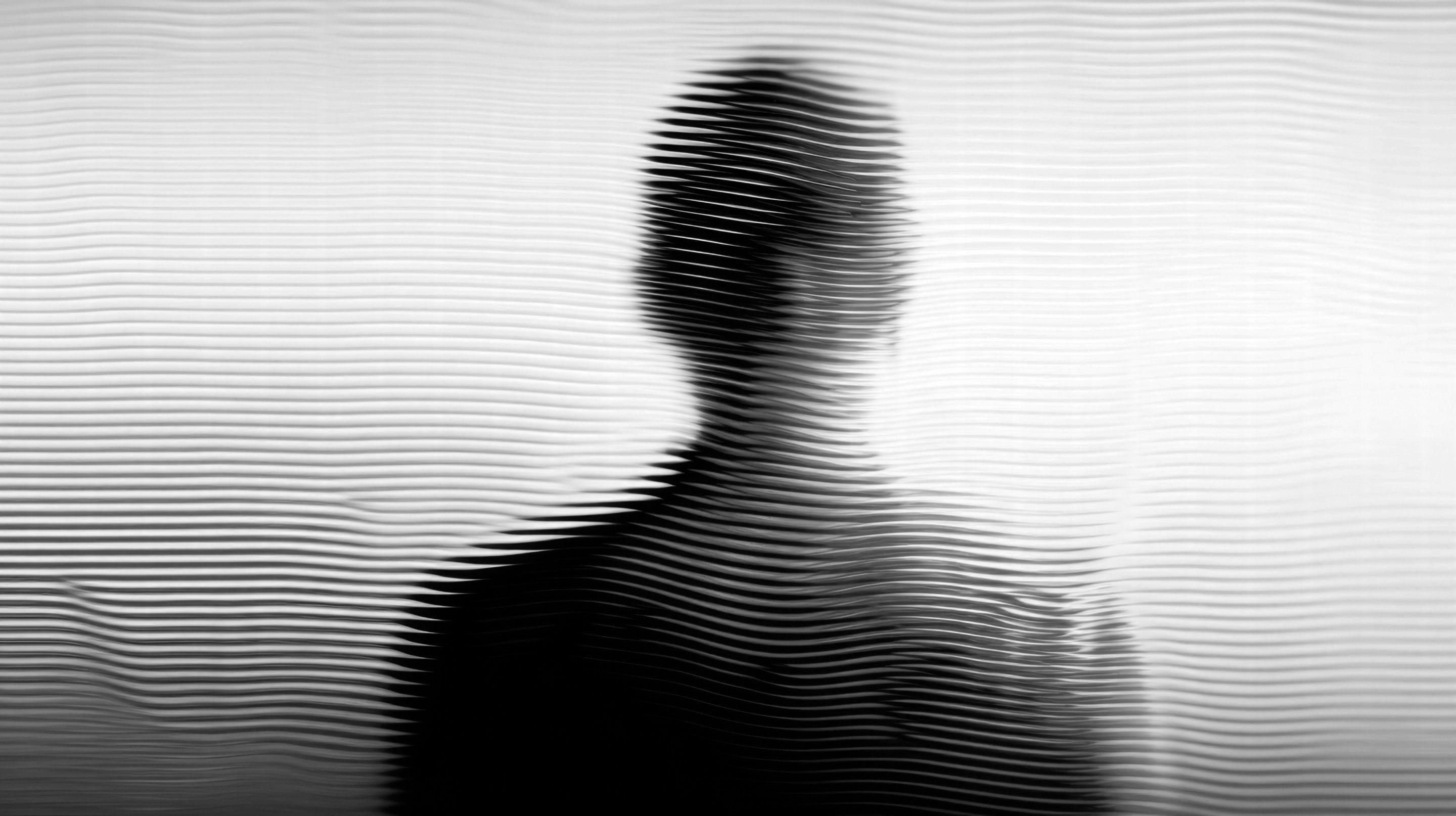 Silhouette eines Mannes hinter geriffeltem Glas, schwarzweiß
